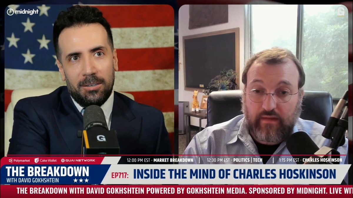The image shows two men sitting at a table with microphones, appearing to be having a conversation or participating in an interview. The background features an American flag, which suggests that this could be taking place during a political event or discussion related to the topic of Charles Hoskinson's statement about the "Inside the Mind of Charles Hoskinson".