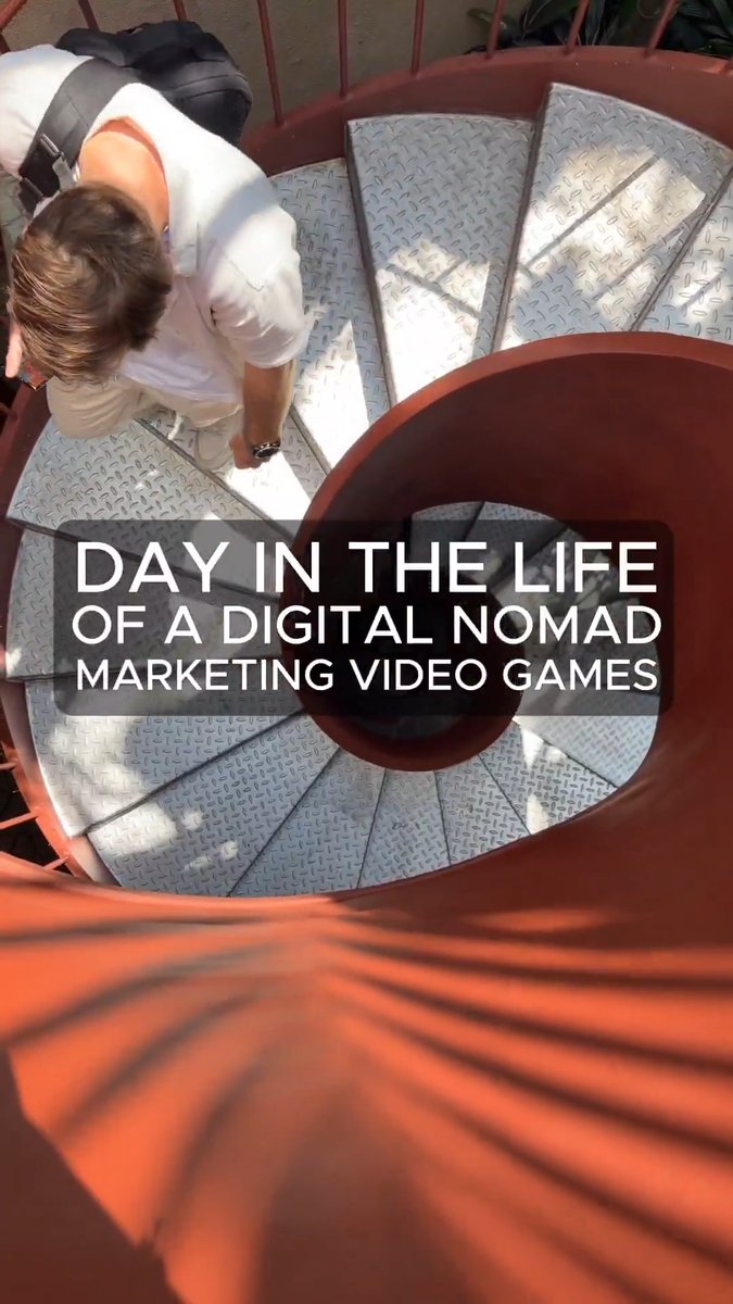 The image shows a person standing at the top of a spiral staircase, with their back facing the camera. The stairs are red and white, adding a pop of color to the scene. Below them, there's text that reads "Day in the life of a digital nomad marketing video games @ AxieInfinity edition". This suggests that the person is likely involved in the world of digital nomadism or video game marketing, as they are standing on top of a spiral staircase with their back to the camera.
