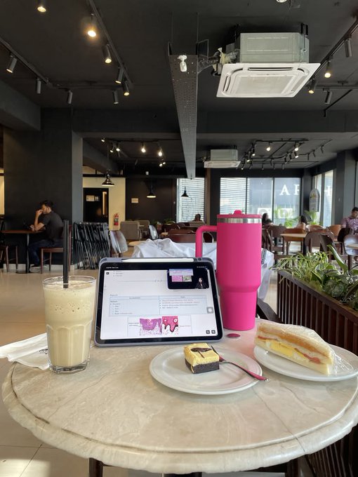 A casual café scene featuring a marble table with a creamy drink, a chocolate dessert, a sandwich, a tablet displaying what appears to be a document, and a bright pink tumbler—paired with a "GM CT" Friday crypto post wishing the community an energetic close to the week, the relaxed café setting reflecting the laid-back "finish the week strong" vibe of the message.
