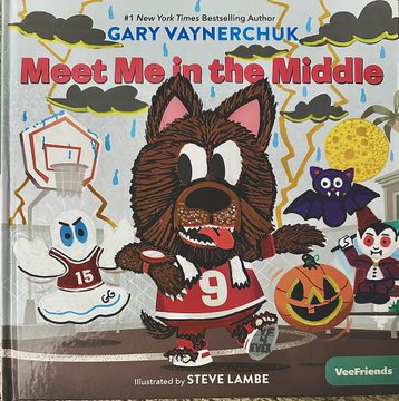 The image is the cover of "Meet Me in the Middle," a children's book by #1 New York Times bestselling author Gary Vaynerchuk, illustrated by Steve Lambo, featuring a basketball-playing wolf character in jersey number 9 alongside VeeFriends characters like a ghost, bat, vampire, and jack-o'-lantern. The caption describes a VeeFriends fan showcasing their first-ever book remark, with the spooky, Halloween-themed cover perfectly matching their costume choice.