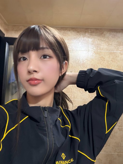 A young woman in a black jacket featuring the yellow "BINANCE" logo takes a selfie while posing with her hand behind her head, humorously pairing with the caption's boast about shorting ZEC (Zcash) at $1107 to fund a house, car, and wife.
