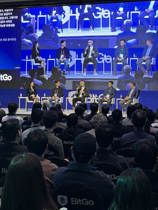 A panel discussion at a BitGo conference features five speakers seated on stage in front of a large screen, while an audience watches, with the post commenting on Korean crypto investors failing to recognize the significance of financial innovations like those discussed at events like this.