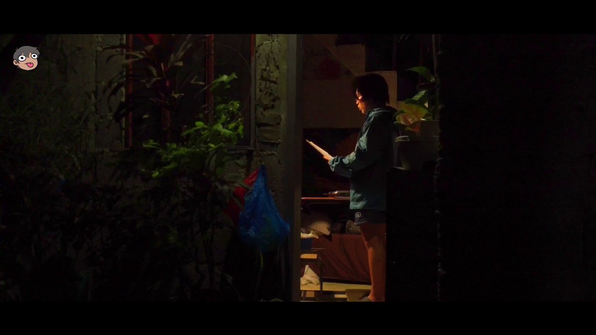 The image shows a person standing outside at night with their back turned towards the camera. The person appears to be reading something, possibly a book or a newspaper, as they are holding an object that resembles a newspaper or a magazine. The background of the photo is dark and out of focus, which emphasizes the subject in the foreground.