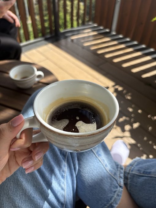 A hand holds a nearly empty coffee cup on a sunlit deck, with a second cup resting on the table, capturing a relaxed Saturday morning moment that contrasts with the post's message about Cryptographic Provenance and verifiable data origins—juxtaposing a casual, trusted daily ritual with the need for trust and verification in physical AI data.