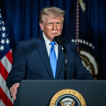 Donald Trump stands at a podium bearing the Presidential Seal, addressing an audience with a serious expression as he speaks into a microphone. The image relates to the post by showing the President during a White House meeting where he urged Congress to pass a "fair version" of the CLARITY Act in discussions with cryptocurrency industry leaders.