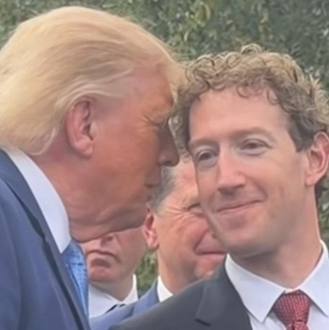 A photo of Donald Trump speaking closely to Mark Zuckerberg at an outdoor event, with other people visible in the background.