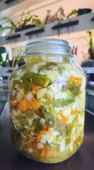 A glass jar filled with a colorful salad mixture of chopped vegetables, herbs, and grains sits on a dark wooden surface.