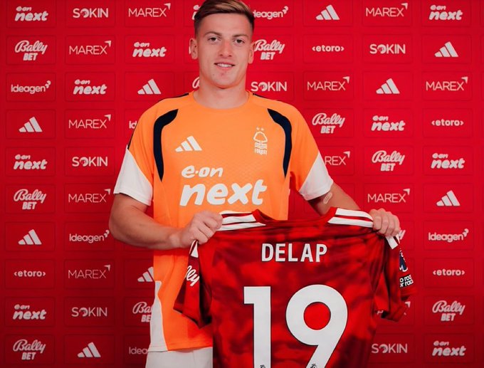 Football player Delap poses in an orange eon next jersey while holding up a red jersey with 'DELAP' and the number 19, standing in front of a red sponsor backdrop featuring Adidas, MAREX, Bally BET, SOKIN, and eToro logos.