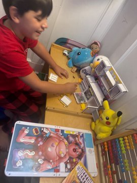 A young boy in a red shirt excitedly opens a large cardboard box filled with a colorful assortment of VeeFriends toys, including plush characters and activity sets. The image captures his joyful unboxing moment, matching the caption celebrating him as a "business. MAN" receiving an array of new merchandise.