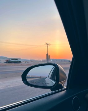 A scenic view of a sunset over a snowy landscape, seen through a car window with the side mirror visible.
