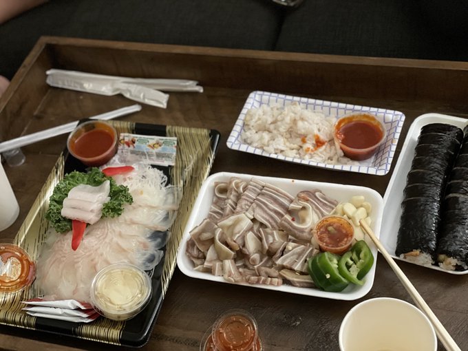 The image shows a takeout meal with what appears to be pork belly slices with peppers and garlic, a plate of white rice with sweet chili sauce, nori-wrapped kimbap rolls, and small containers of dipping sauces, served on a wooden tray with chopsticks. The caption humorously contrasts this modest meat-focused meal with "natural fresh sashimi," using the joke to playfully solicit TRON cryptocurrency donations.