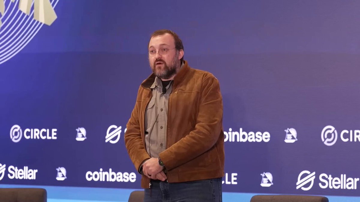 The image features a man wearing a brown jacket standing in front of a blue wall with white logos for Circle, Stellar, and Coinbase. The man appears to be giving a speech or presentation at an event.