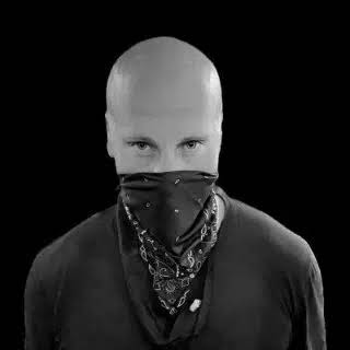A bald man wearing a black shirt and a bandana covering the lower half of his face stares intensely at the camera, his piercing eyes giving him a menacing appearance that matches the darkly humorous caption about committing crimes.