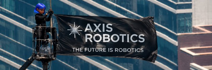 A person in a blue helmet stands on a suspended platform holding a black banner reading 'AXIS ROBOTICS - THE FUTURE IS ROBOTICS' in front of a modern glass building.