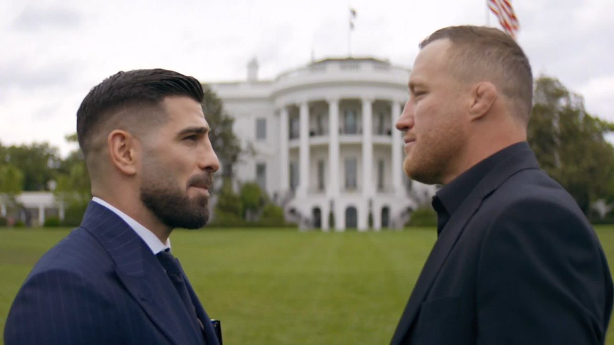 The image shows two men dressed in suits standing next to each other, facing off against a backdrop of the White House. The man on the left has his back turned towards the camera while the man on the right faces directly at the viewer. Both men are wearing ties and appear to be engaged in a serious conversation or discussion.
