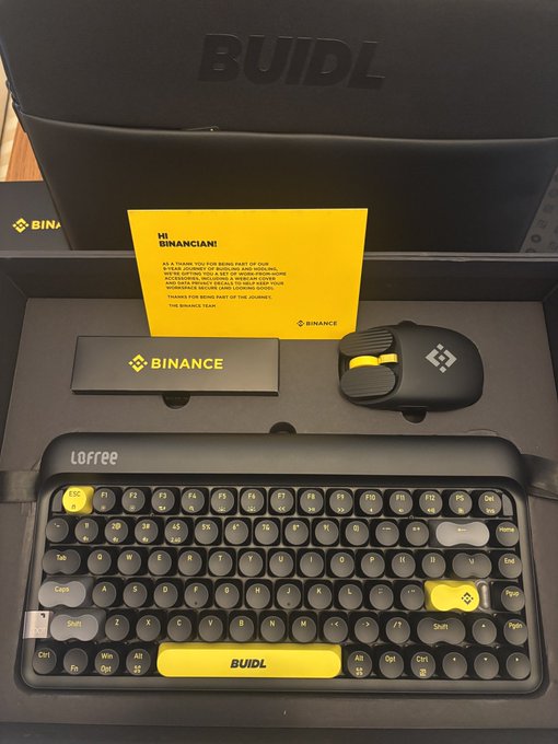 A Binance-branded Lofree mechanical keyboard with round keycaps and a matching mouse are displayed in a "BUILDL" gift box, featuring a yellow "Hi Binancian!" card from The Binance Team thanking the recipient for being part of their Web3 journey. The setup aligns perfectly with the celebratory GM post showcasing the long-awaited 9YA Binance merchandise gift.