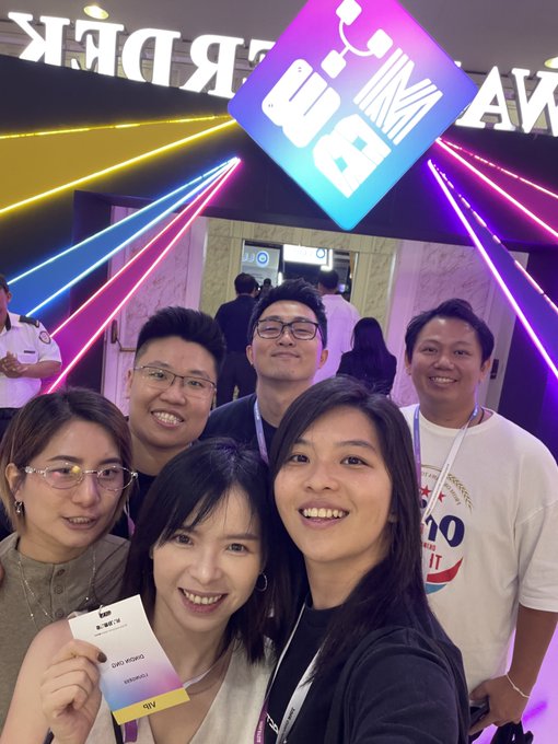 Group selfie of six smiling people posing under a neon 'MiMi Awards' sign with colorful laser lights, with one woman holding a VIP attendee badge.