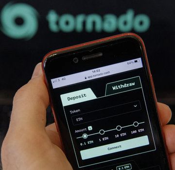 A hand holds a smartphone displaying the Tornado Cash app interface with deposit and withdraw options for ETH tokens, with the "tornado" logo visible in the background. The image visually anchors the article's claim that Tornado Cash's founder Roman Storm argues AI tools from Google and OpenAI are being misused to fund North Korea's nuclear program, illustrating the crypto privacy tool central to the discussion.