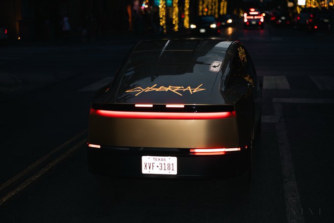 The rear view of a dark sports car with gold 'CYBERBEAST' lettering on the back, displaying a Texas license plate reading 'XVF-3181', parked on a city street at night.