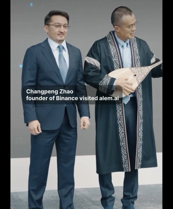 The image shows two men standing together; one is Changpeng Zhao, founder of Binance, wearing a dark suit, and the other is dressed in a traditional Kazakh "Chapan" robe featuring ornate embroidered borders, holding a decorative dombra instrument. Text overlay reads "Changpeng Zhao founder of Binance visited alem.ai," which aligns with the post's caption noting that the traditional Kazakh Chapan looks great on CZ while referencing his visit to the Kazakh AI company Alem.ai.