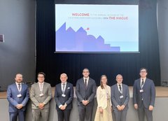 Seven formally dressed individuals stand on a stage in front of a large presentation screen displaying a "WELCOME" slide that reads "The world of MAGUS" along with event details, while the accompanying post context discusses topics including the Revolut breach, weaponized compliance culture, and transnational financial repression as explained by Lyudmyla Kozlovska.