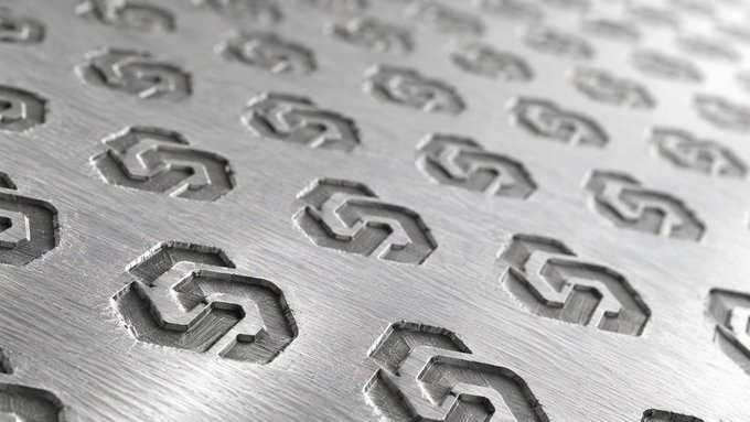 A close-up, angled photograph of a brushed metal surface featuring a repeating pattern of embossed, stylized hexagonal 'S' logos.