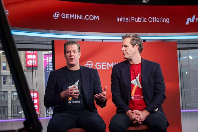 Two men sit side by side in front of a red backdrop displaying "GEMINI.COM," "Initial Public Offering," and the Nasdaq logo, with one man holding a commemorative crystal trophy during what appears to be a post-IPO interview broadcast. The accompanying post about Gemini stock plummeting roughly 80% since its listing, leaving its market cap at around $753 million versus a previous peak of nearly $4 billion, contextualizes this scene as a stark contrast to the celebratory IPO moment captured, highlighting the dramatic decline the cryptocurrency exchange has experienced since the founders' early public appearance.