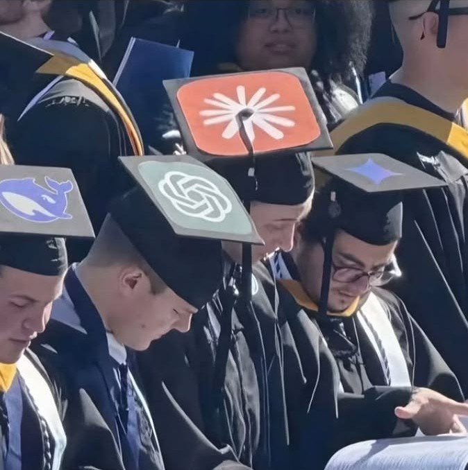 Photo of graduating students in caps and gowns, with several mortarboards decorated with AI company logos including Anthropic (claude logo), OpenAI (starburst logo), and a whale logo.