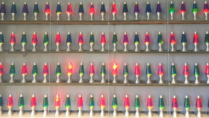 Multiple shelves display rows of vintage lava lamps in white bases with colorful blobs (pink, green, blue, purple) illuminated from within.
