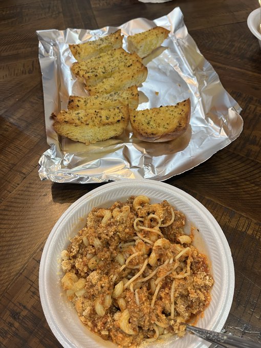 Garlic bread slices on foil and a bowl of spaghetti with meat sauce and grated cheese sit on a wooden table, matching the cozy, homemade spirit of a "Spaghetti night" dinner.