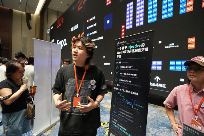 A young person wearing a lanyard speaks at what appears to be an expo, standing next to a display about 'Injective Web3 实体物品贸易交易平台'.