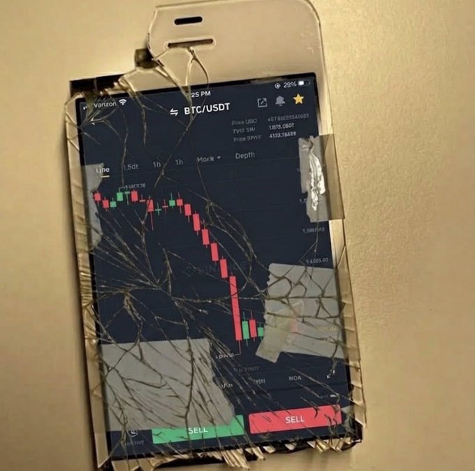 A cracked smartphone displaying a BTC/USDT trading chart showing a dramatic price decline with red and green candlesticks and SELL buttons at the bottom.