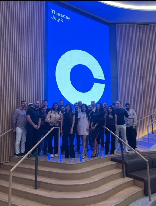 A group of attendees poses together on a curved staircase in front of a large blue screen displaying "Thursday July 9" and a stylized "C" logo, likely at a tech or crypto conference. The caption aligns with the post, which highlights AgenticsCredit's Agentic Credit Score as a way to vet AI trading agents based on performance before allocating capital.
