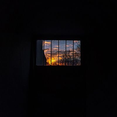 A serene sunset visible through a barred window in a darkened room.