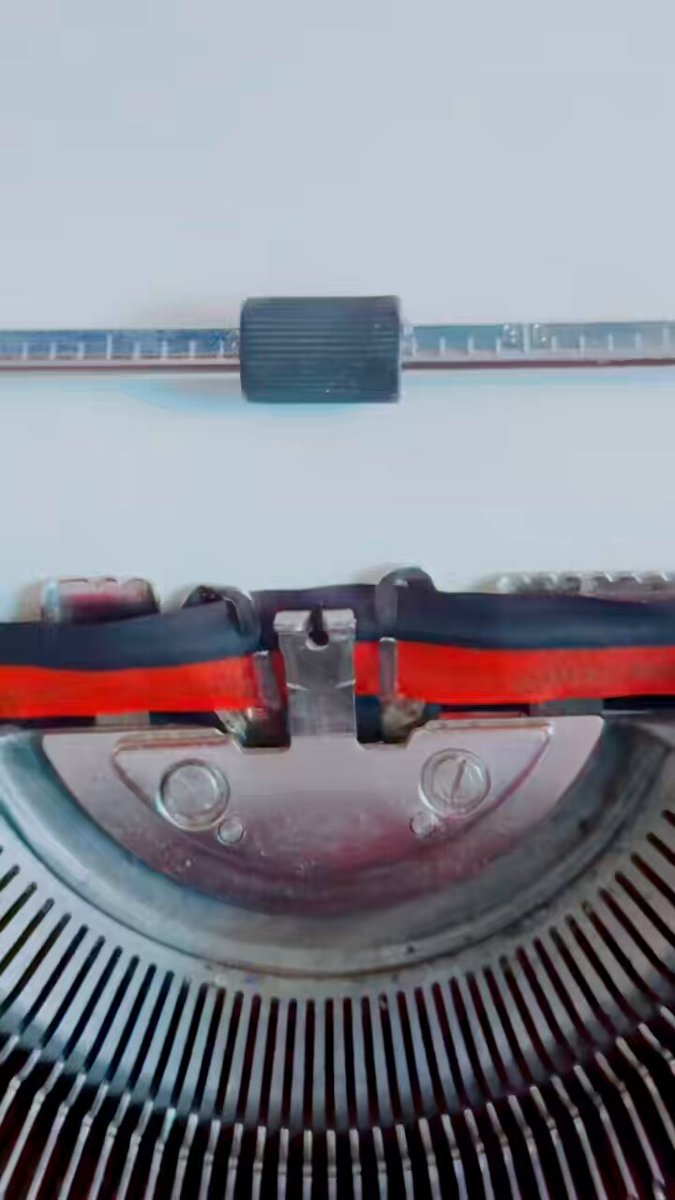 The image shows a close-up view of an old-fashioned, vintage typewriter with black keys and red accents. The typewriter has two large keys that are connected by a small metal piece, which appears to be part of the mechanism responsible for pressing the keys. The background is white, providing a stark contrast that makes the typewriter stand out even more. The image also includes text that reads "1/1 typewriter originals. Own the real thing → degenpoet.com".