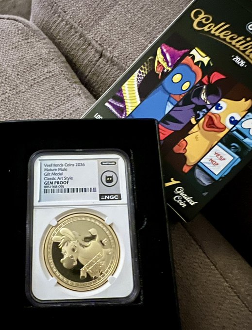A graded 2026 WeeFriends Coins 'Mature Mule' gilt medal (GEM PROOF, NGC certified) in a black display case next to its colorful cartoon-themed collector box.