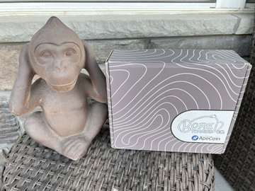 A terracotta monkey figurine sits beside a patterned welcome package labeled "Bored Apes ApeCoin" featuring a topographical wave design, representing the swag received from the @WelcomeApes initiative for Bored Ape Yacht Club owners.