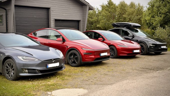 Four parked electric vehicles, including two Tesla models and two other EVs with rooftop cargo boxes, parked on gravel in front of a building.