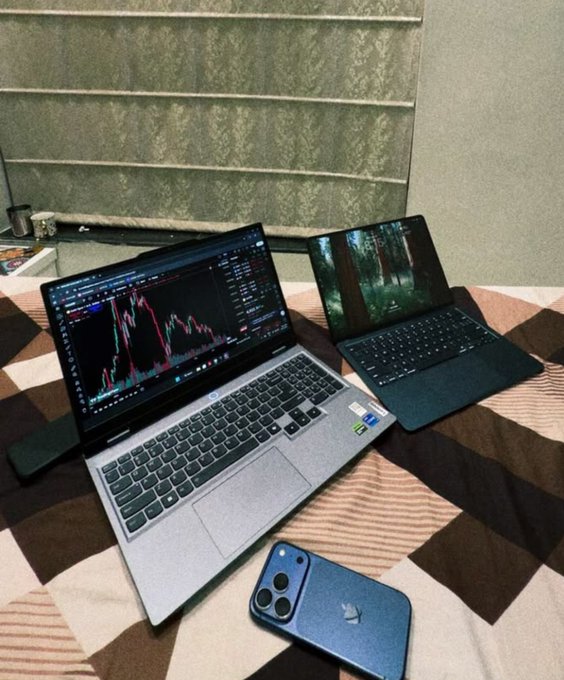 A weekend trading setup featuring two laptops—one displaying a candlestick chart and the other showing a forest wallpaper—alongside an iPhone on a checkered table, perfectly illustrating the "work hard, trade smart, enjoy life" balance mentioned in the post.