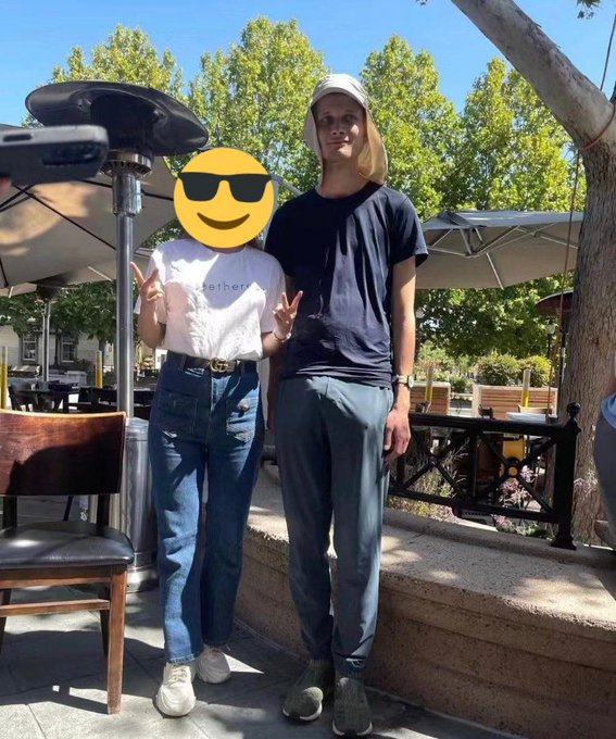 Two people stand outdoors at what appears to be an outdoor dining area, with one person wearing a white 'tether' t-shirt and jeans, and the other in a navy t-shirt and gray sweatpants.