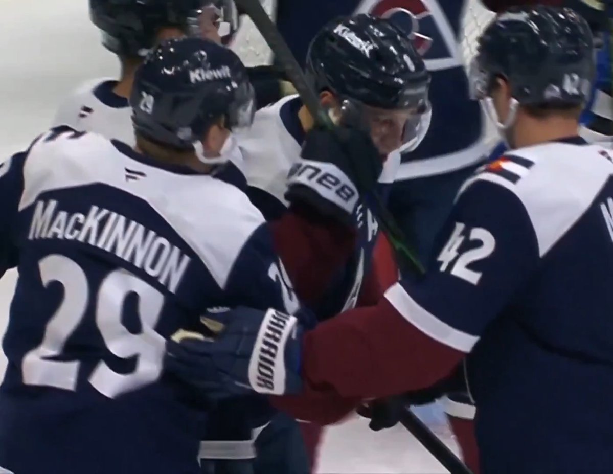 Colorado Avalanche hockey players celebrate on the ice, with 'MacKINNON 29' visible on the back of one player's jersey and '42' on another, along with Bauer Warrior branded equipment.