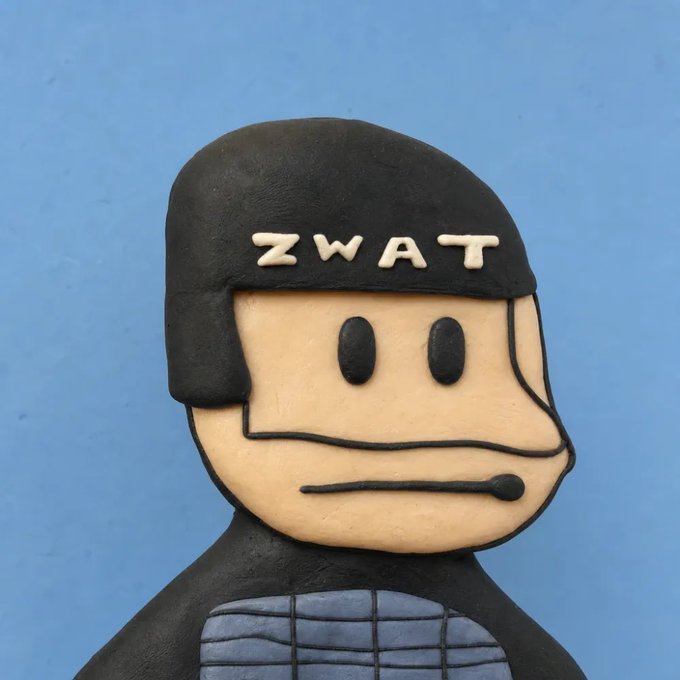 A claymation-style figurine of a character with a serious expression wearing a black helmet labeled 'ZWAT' and a black suit with a blue chest piece, set against a blue background.