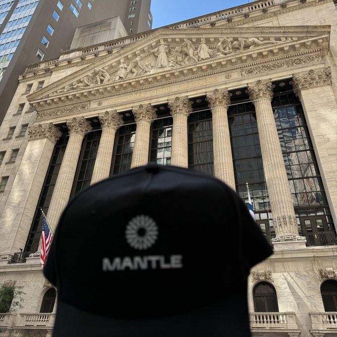 The image features a black baseball cap with the word "MANTLE" written on it, placed in front of a large building that appears to be the New York Stock Exchange (NYSE). The text in the image reads "Insane news coming from Bybit right now as i'am standing in front of NYSE TradFi is moving onchain. And it'S moving fast". This suggests that there might have been some significant financial events or news related to the stock market, causing a flurry of activity and potentially impacting the value of certain stocks.