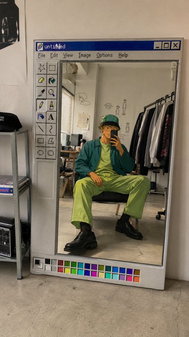 A person taking a mirror selfie reflected in a full-length mirror designed to look like the classic MS Paint interface, with the user wearing a green cap and bright green outfit.