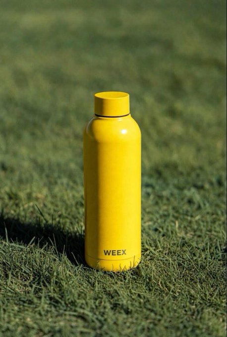 A yellow "WEEX" branded water bottle sits upright on green grass, fitting the post's "touching grass" theme with a sunny outdoor vibe.