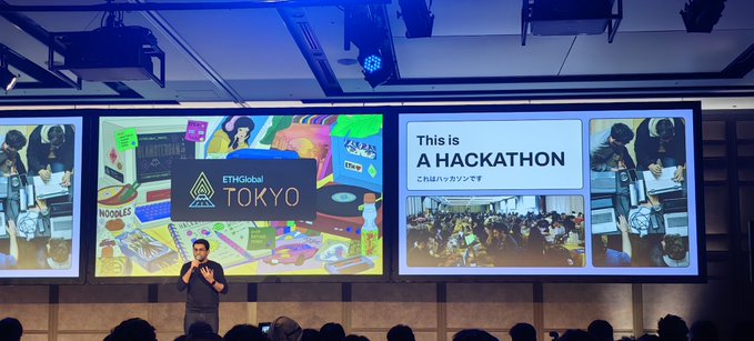 A man presenting at the "ETHGlobal TOKYO" hackathon event, with slides displaying "This is A HACKATHON" and "ETHGlobal TOKYO" on large screens behind him.