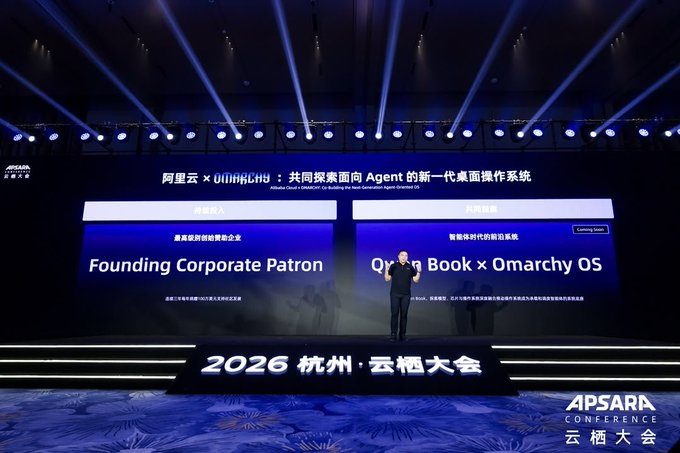 A stage presentation at the 2026 APSARA Conference (杭州·云栖大会) showing Alibaba Cloud × OMARCHY announcing their partnership, with a presenter standing on stage before a screen displaying 'Founding Corporate Patron' and 'Qwen Book × Omarchy OS'.
