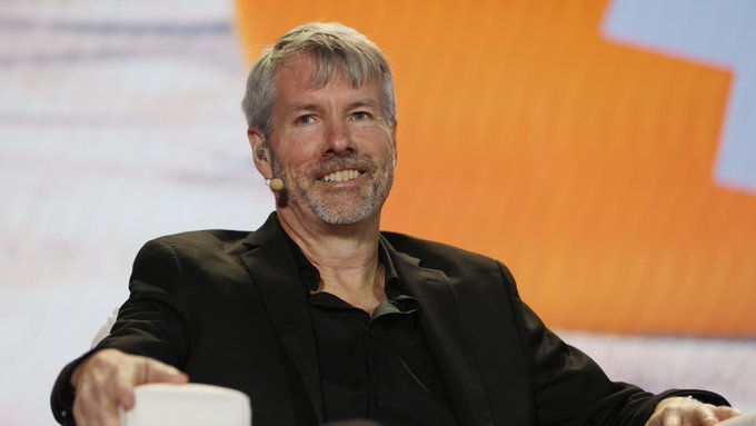 Michael Saylor, executive chairman of Strategy (formerly MicroStrategy), smiles while wearing a headset microphone at what appears to be a conference, in connection with news that Strategy may sell up to $5 billion worth of Bitcoin following a reported $8.2 billion Q2 loss.