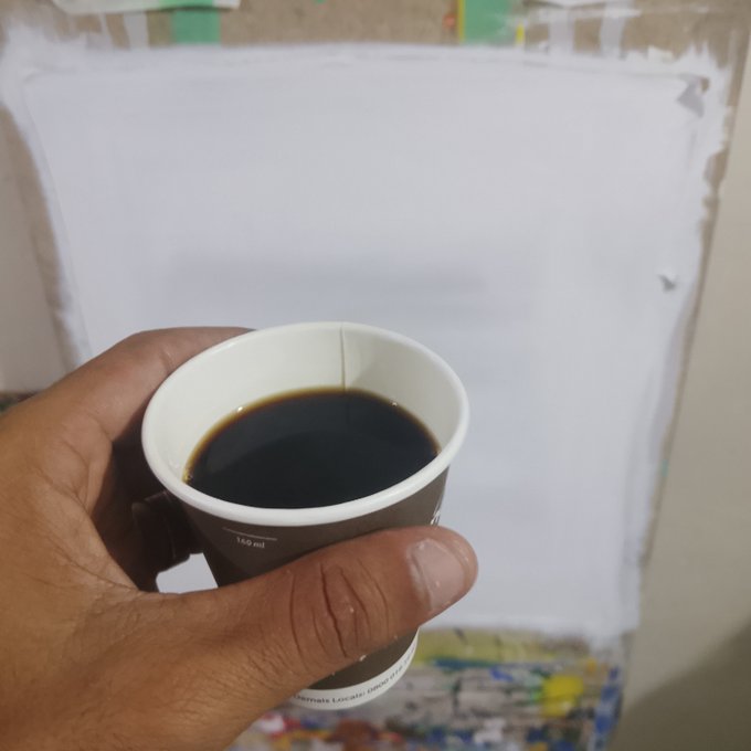 A hand holding a small paper cup filled with black coffee, marked '160 ml' and 'Alternate Locate non-caf', held up in front of an unfinished white painting on a canvas.