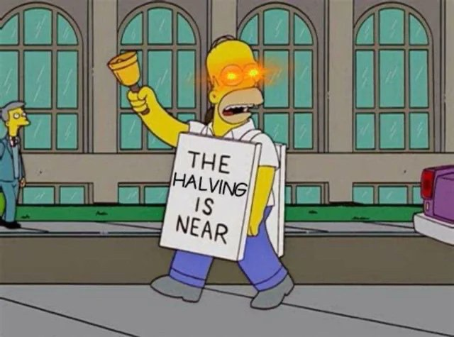 The Simpsons meme featuring Homer with glowing red eyes holding a bell, wearing a sign that reads "THE HALVING IS NEAR," referencing the Bitcoin halving event.